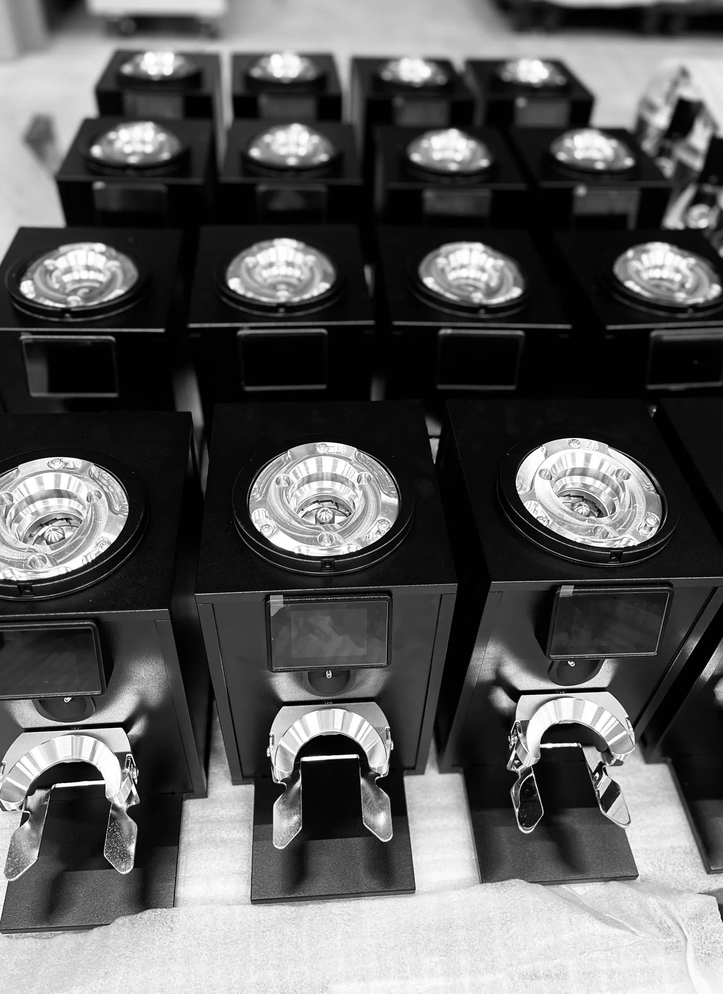 Black-and-white photo from above of rows of Bentwood H75 grinder bodies, without hoppers, their machined burr carriers and portafilter forks catching the light